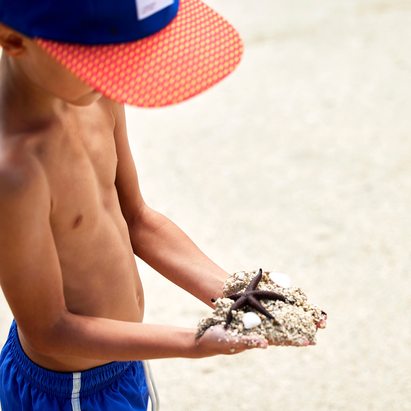 child holding sand and starfish in hand